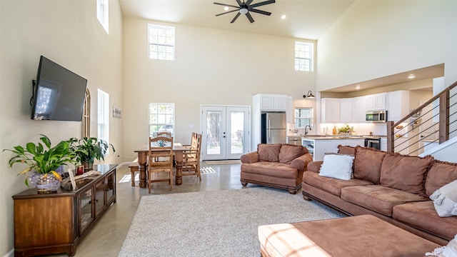 living area featuring a healthy amount of sunlight, a ceiling fan, finished concrete floors, a towering ceiling, and stairs