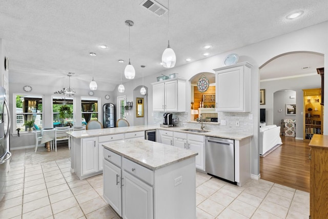 kitchen with a peninsula, stainless steel dishwasher, a sink, arched walkways, and visible vents
