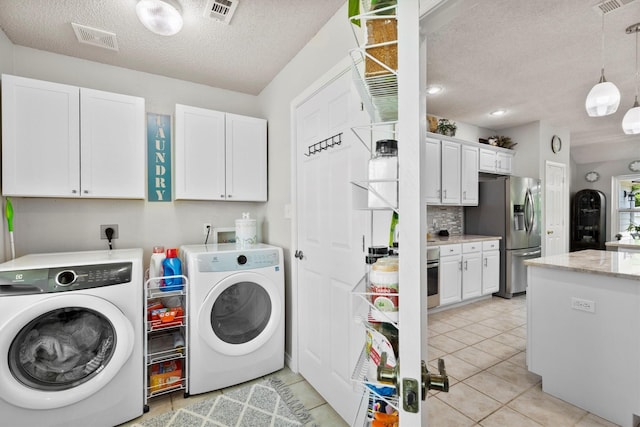washroom featuring washing machine and dryer, visible vents, a textured ceiling, and cabinet space