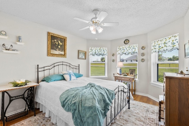 bedroom featuring baseboards, a textured ceiling, light wood-style floors, and ceiling fan