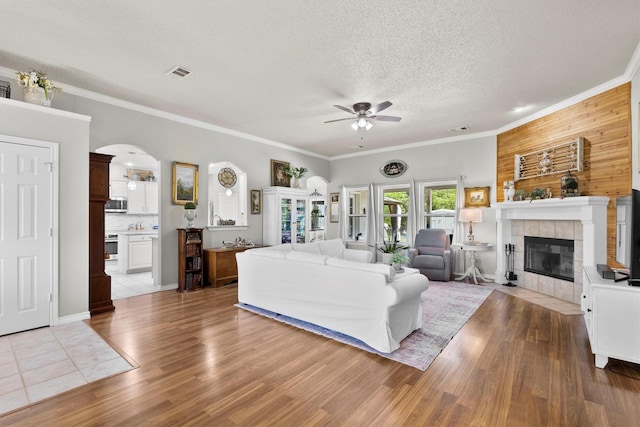 living area with a ceiling fan, wood finished floors, arched walkways, a fireplace, and visible vents