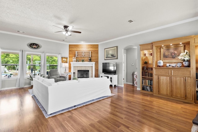 living area with arched walkways, visible vents, baseboards, a ceiling fan, and a tile fireplace
