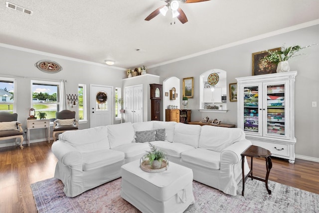 living room with wood finished floors, ceiling fan, arched walkways, ornamental molding, and visible vents