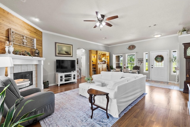 living area with ceiling fan, crown molding, a tile fireplace, and visible vents