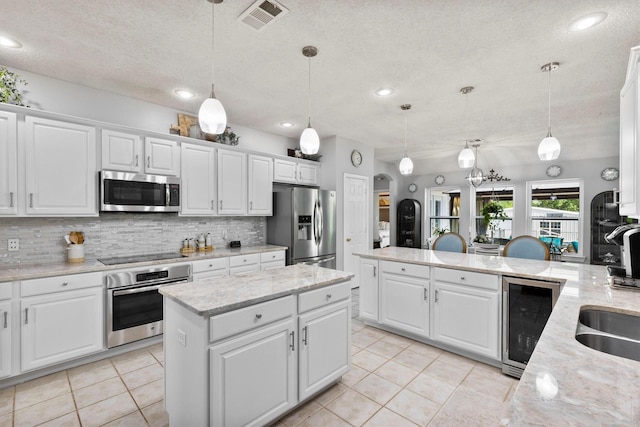 kitchen featuring a textured ceiling, stainless steel appliances, backsplash, wine cooler, and visible vents