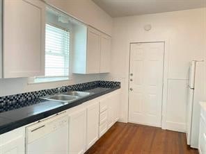 kitchen with dark wood-style flooring, white appliances, a sink, white cabinetry, and dark countertops