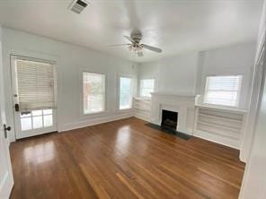 unfurnished living room with wood finished floors, visible vents, ceiling fan, baseboards, and a fireplace with flush hearth