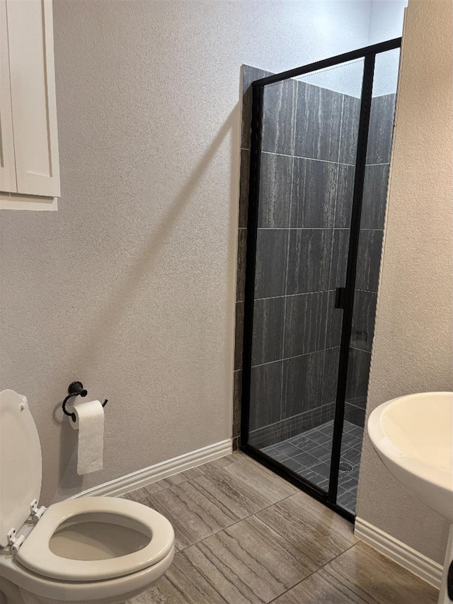 bathroom featuring baseboards, a textured wall, toilet, and a stall shower