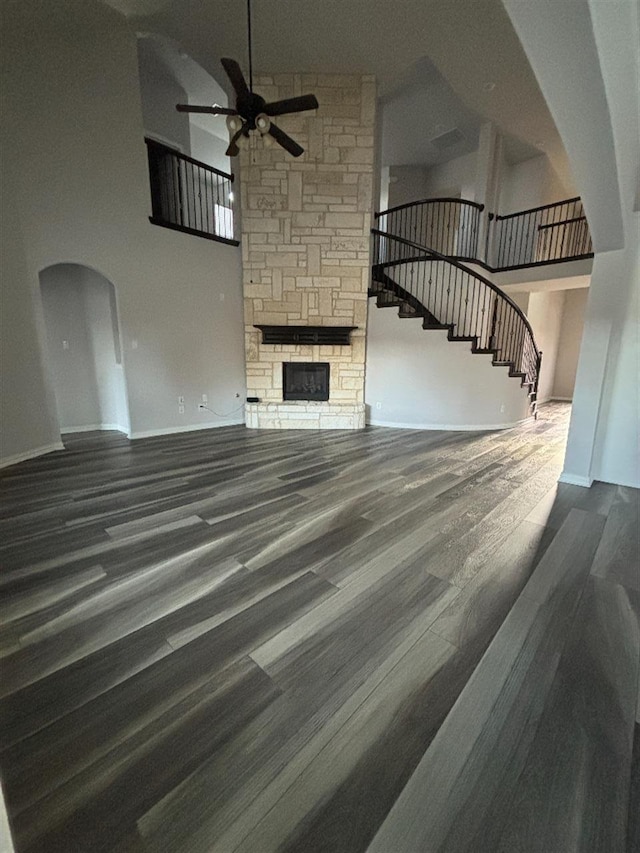 unfurnished living room featuring arched walkways, ceiling fan, a fireplace, stairway, and a towering ceiling