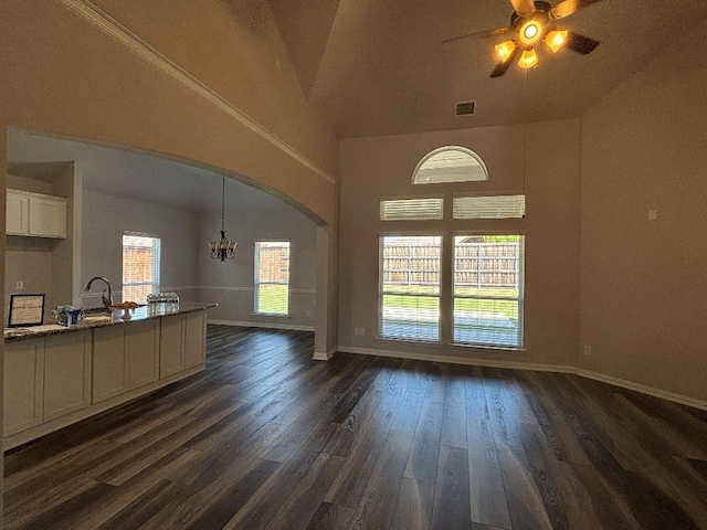 unfurnished living room featuring arched walkways, ceiling fan with notable chandelier, baseboards, and a healthy amount of sunlight