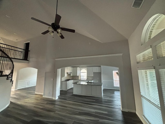 unfurnished living room featuring dark wood-style floors, a ceiling fan, visible vents, high vaulted ceiling, and arched walkways