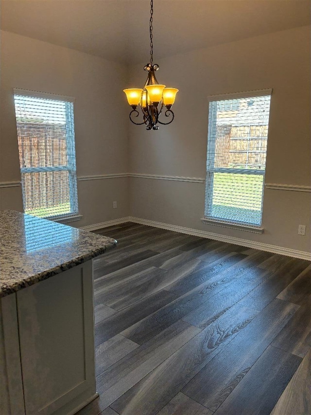 unfurnished dining area featuring a healthy amount of sunlight, an inviting chandelier, baseboards, and dark wood finished floors