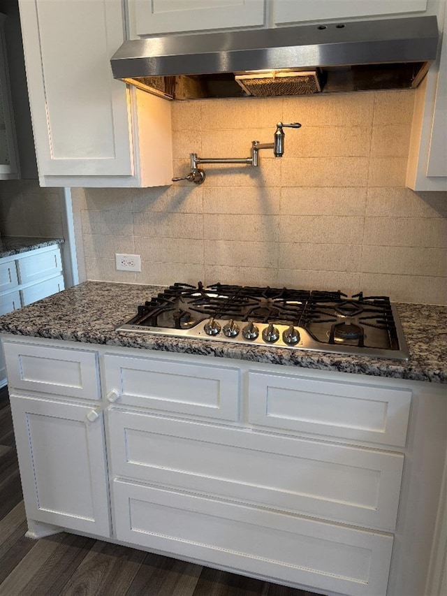kitchen featuring dark stone countertops, tasteful backsplash, under cabinet range hood, white cabinetry, and stainless steel gas cooktop