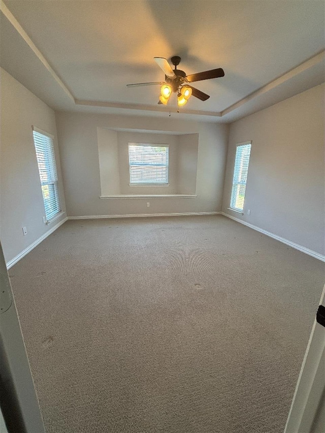 unfurnished room with a wealth of natural light, ceiling fan, baseboards, and a raised ceiling