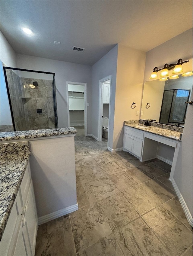 bathroom featuring vanity, baseboards, a spacious closet, a shower stall, and visible vents