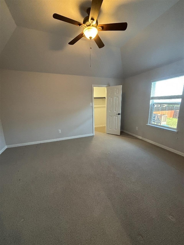unfurnished bedroom with baseboards, carpet flooring, a ceiling fan, a walk in closet, and lofted ceiling