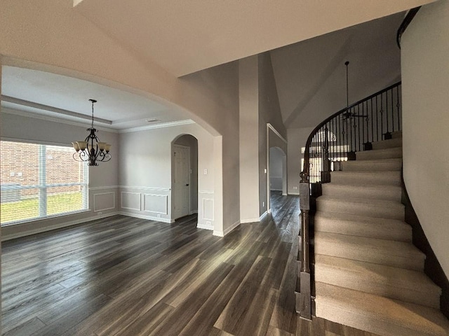 stairway featuring arched walkways, wood finished floors, an inviting chandelier, and a decorative wall