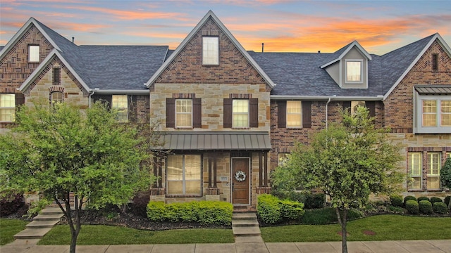 view of property featuring stone siding, a lawn, roof with shingles, and brick siding