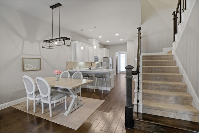 dining area with stairs, arched walkways, dark wood finished floors, baseboards, and recessed lighting