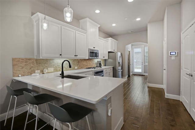 kitchen featuring arched walkways, a sink, baseboards, light countertops, and appliances with stainless steel finishes