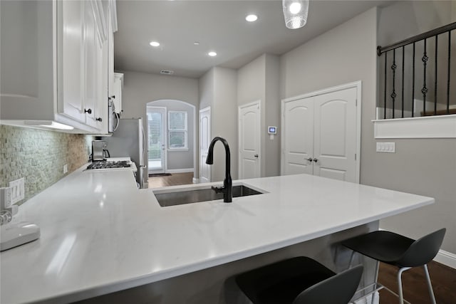kitchen with a sink, decorative backsplash, arched walkways, a peninsula, and dark wood-style flooring