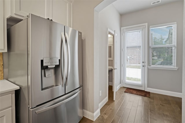 kitchen with white cabinets, stainless steel refrigerator with ice dispenser, wood finished floors, and baseboards