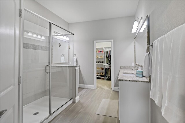 full bath with a stall shower, baseboards, a spacious closet, vanity, and wood finish floors