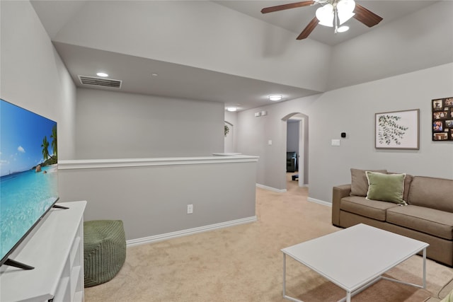 living area with a ceiling fan, arched walkways, light carpet, a towering ceiling, and visible vents