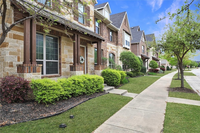 property entrance with a shingled roof, a yard, a residential view, stone siding, and brick siding