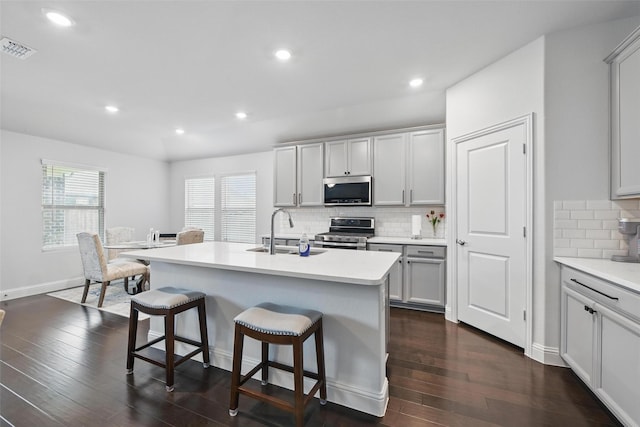 kitchen with dark wood-style floors, visible vents, a kitchen bar, stainless steel appliances, and a sink
