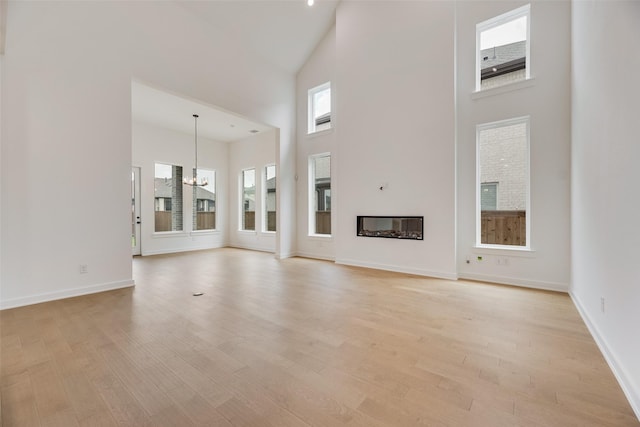 unfurnished living room with light wood-type flooring, baseboards, a towering ceiling, and a notable chandelier