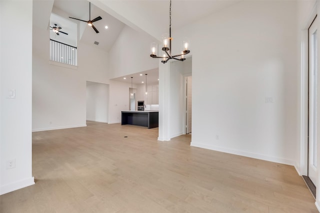unfurnished living room featuring baseboards, high vaulted ceiling, ceiling fan with notable chandelier, and light wood-style floors