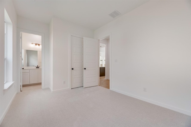 unfurnished bedroom featuring visible vents, a closet, light carpet, baseboards, and ensuite bath