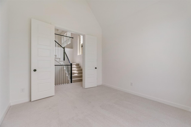 unfurnished room with stairway, baseboards, lofted ceiling, and light colored carpet