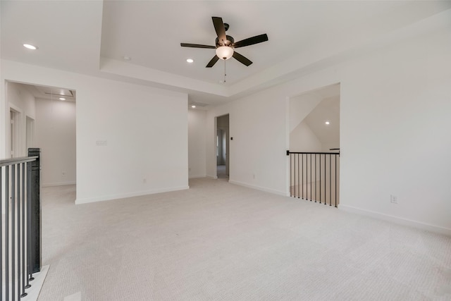 unfurnished room featuring light colored carpet, attic access, a ceiling fan, recessed lighting, and a tray ceiling
