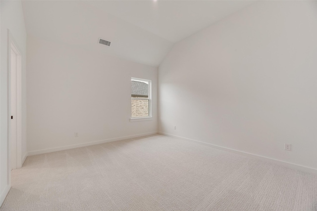 spare room with baseboards, lofted ceiling, light colored carpet, and visible vents