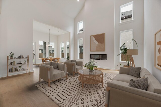living area with a notable chandelier, light wood-style floors, high vaulted ceiling, a glass covered fireplace, and baseboards