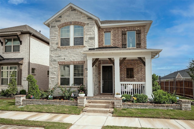 view of front of house with brick siding, a porch, stone siding, and fence