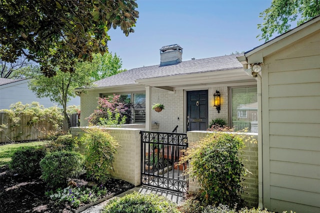 property entrance featuring brick siding, fence, a gate, a chimney, and a shingled roof