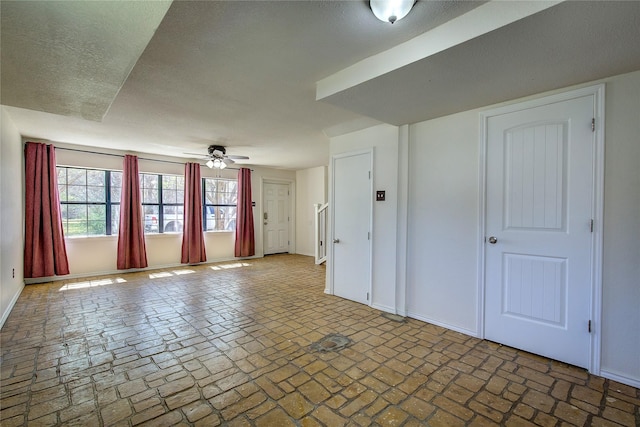 interior space featuring brick floor, baseboards, a ceiling fan, and a textured ceiling