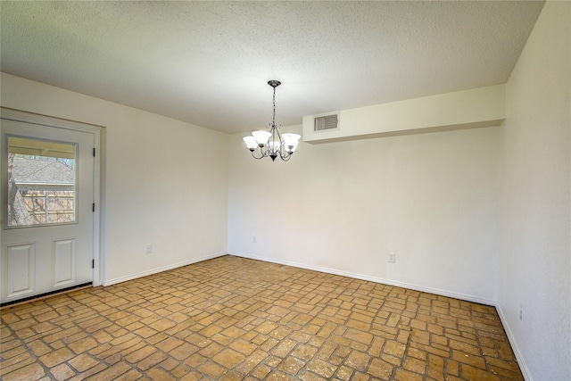 spare room with visible vents, baseboards, a notable chandelier, a textured ceiling, and brick floor