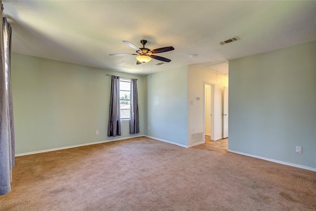 empty room with visible vents, a ceiling fan, attic access, and light colored carpet