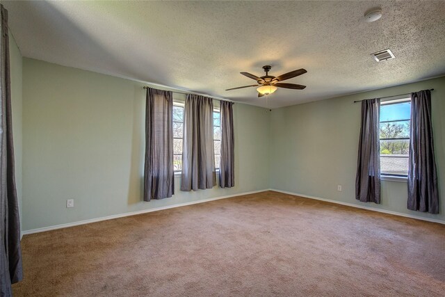 empty room featuring a textured ceiling, ceiling fan, visible vents, and carpet floors