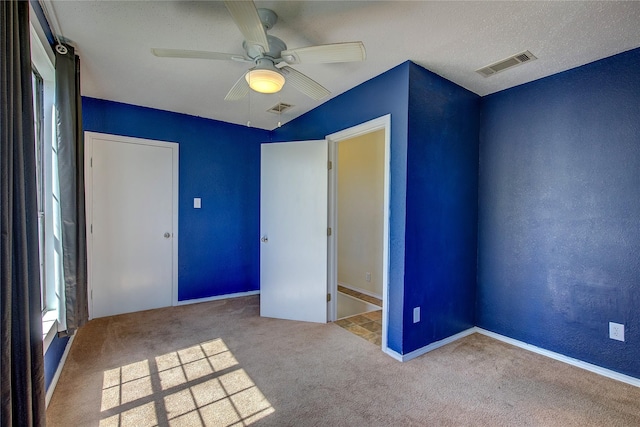 unfurnished bedroom featuring visible vents, a textured wall, a ceiling fan, and carpet floors