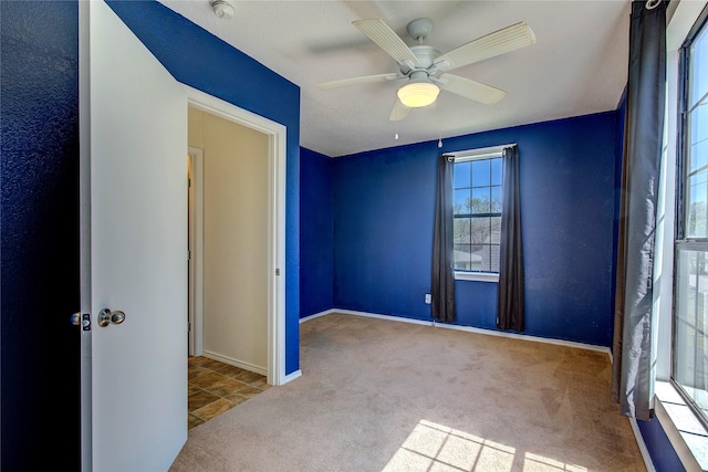 carpeted spare room featuring baseboards and ceiling fan