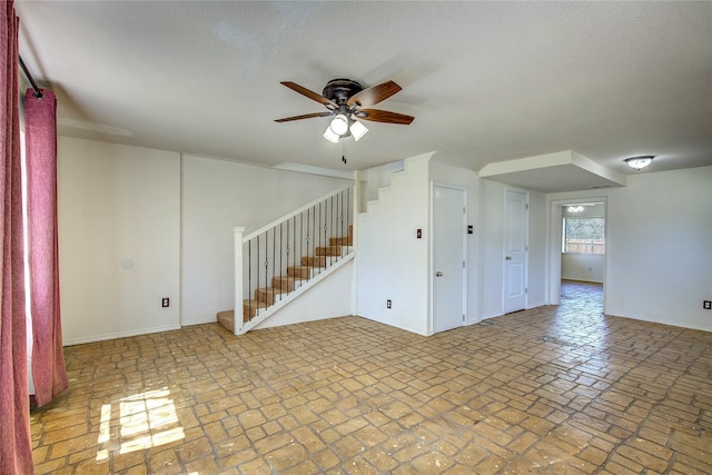 unfurnished room with ceiling fan, brick floor, baseboards, and stairs