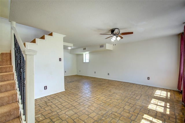 spare room with baseboards, stairway, visible vents, ceiling fan, and brick floor