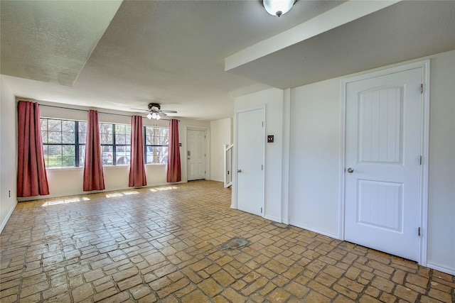 unfurnished living room featuring brick floor, ceiling fan, baseboards, and a textured ceiling