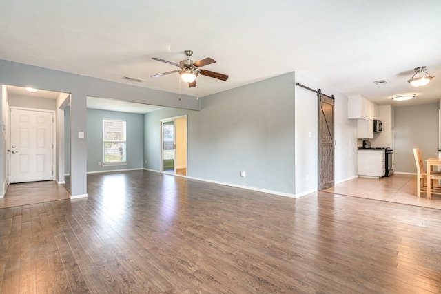 unfurnished living room featuring baseboards, a barn door, visible vents, ceiling fan, and wood finished floors