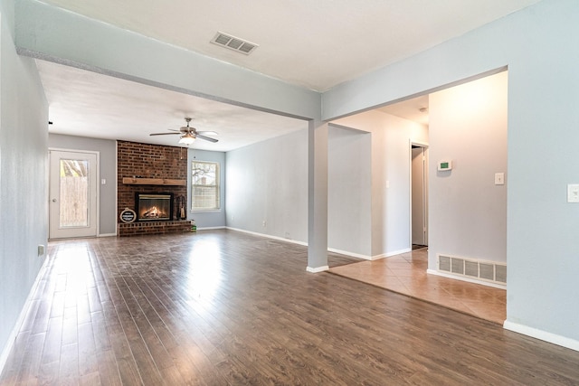 unfurnished living room featuring visible vents, a brick fireplace, a ceiling fan, and wood finished floors
